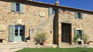 A stone building with a tiled roof, multiple windows with shutters, and a central staircase leading to a door.