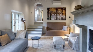 A spacious living room with a fireplace, a sofa, a coffee table, and a patterned ottoman.