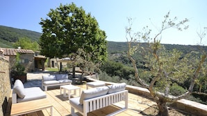 A wooden deck with outdoor furniture, a stone building, and a view of a hilly landscape.