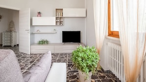 Un salon moderne avec un téléviseur à écran plat, des étagères intégrées, un canapé gris et une plante en pot.