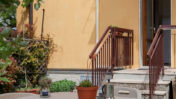 Une terrasse extérieure avec une table dressée pour deux personnes, entourée de plantes en pot et d’un escalier.
