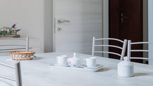 Une table à manger avec des chaises blanches, un panier et un service à thé blanc.