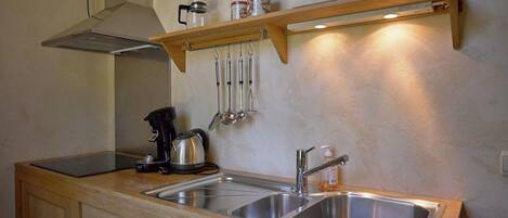 A compact kitchen with a sink, a kettle, and a coffee maker. There are wooden cabinets and a shelf above the sink.