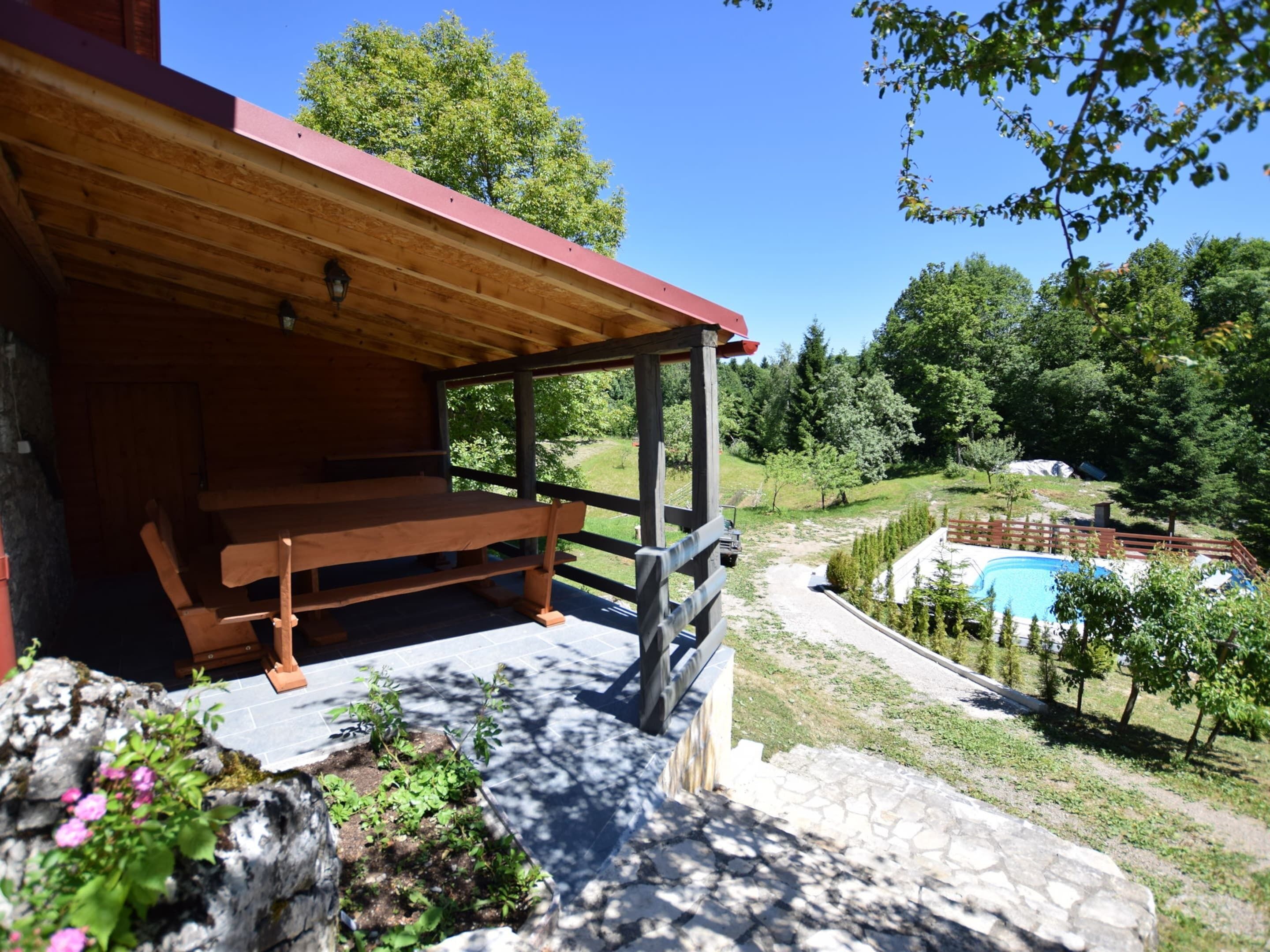 A wooden cabin with a bench and a stone pathway leading to a swimming pool surrounded by trees.