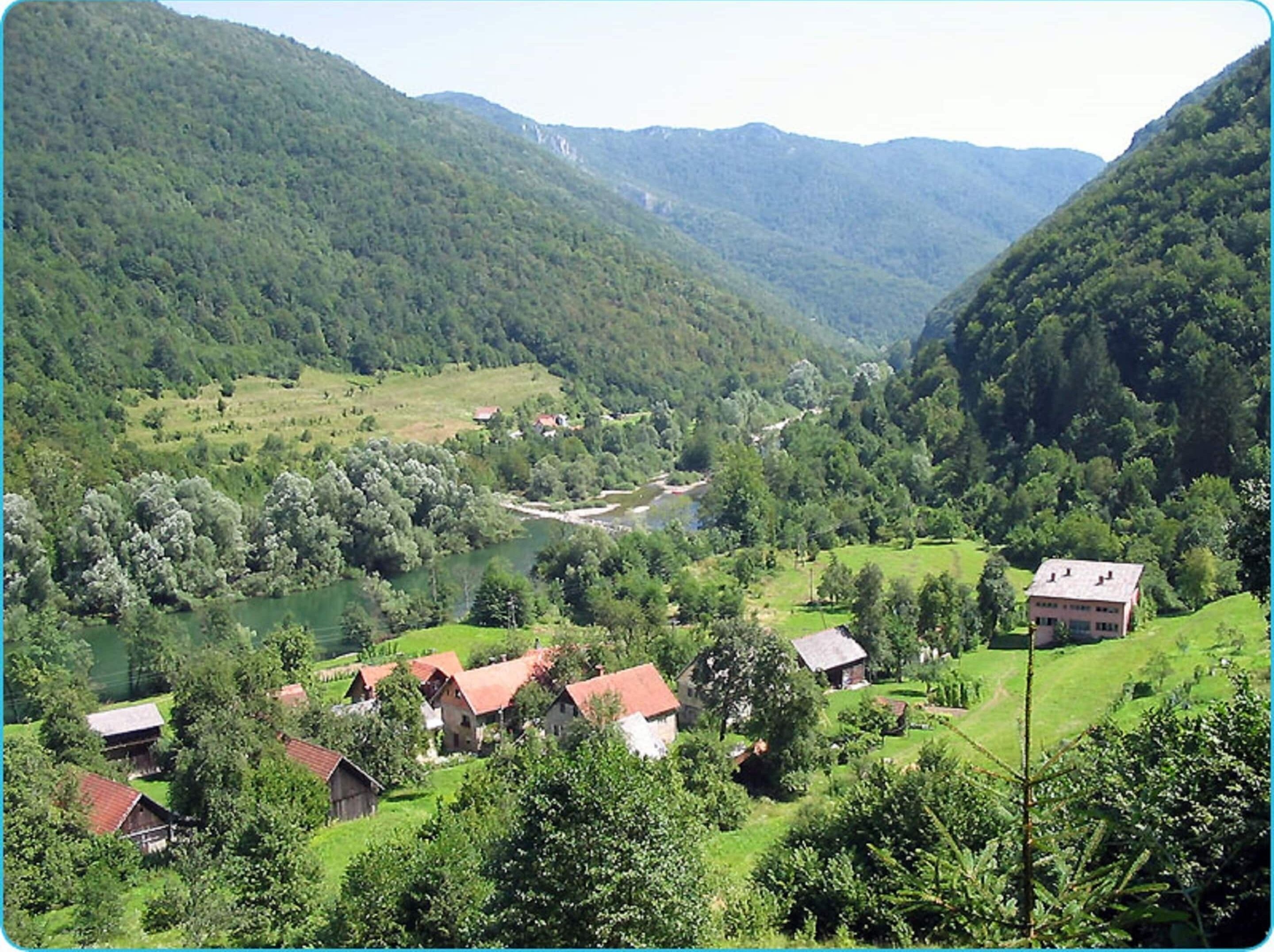 Ländliche Landschaft mit Fluss, Häusern und umgebender Vegetation.