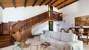 A spacious living room with a white sofa, a wooden staircase, and a dining area with chairs and a table. - Belvilla by OYO Gira Sole (Syracuse)