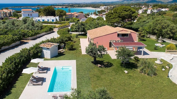 A residential area with a swimming pool, a large house with a red roof, and a view of the sea and mountains in the background. - Belvilla by OYO Gira Sole (Syracuse)