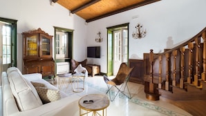A spacious living room with a white sofa, a wooden cabinet, a round table, and a staircase. - Belvilla by OYO Gira Sole (Syracuse)