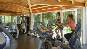 Ein Fitnessraum mit Laufbändern und Kraftgeräten, Holzbalken an der Decke und großen Fenstern mit Blick auf Bäume.