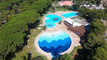 Vista aérea de um resort com várias piscinas, rodeado por vegetação exuberante e alguns edifícios.