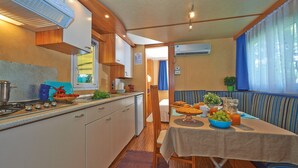 A compact kitchen with a stove, sink, and a dining area with a table set for breakfast. - Beach Chalet + Pool & Veranda (Cellole)