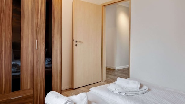 A bedroom with two beds, a wooden wardrobe, and a door leading to another room. - Snug Apartment in Kalkhorst with Terrace near City Center (Kalkhorst)