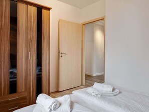 A bedroom with two beds, a wooden wardrobe, and a door leading to another room. - Snug Apartment in Kalkhorst with Terrace near City Center (Kalkhorst)