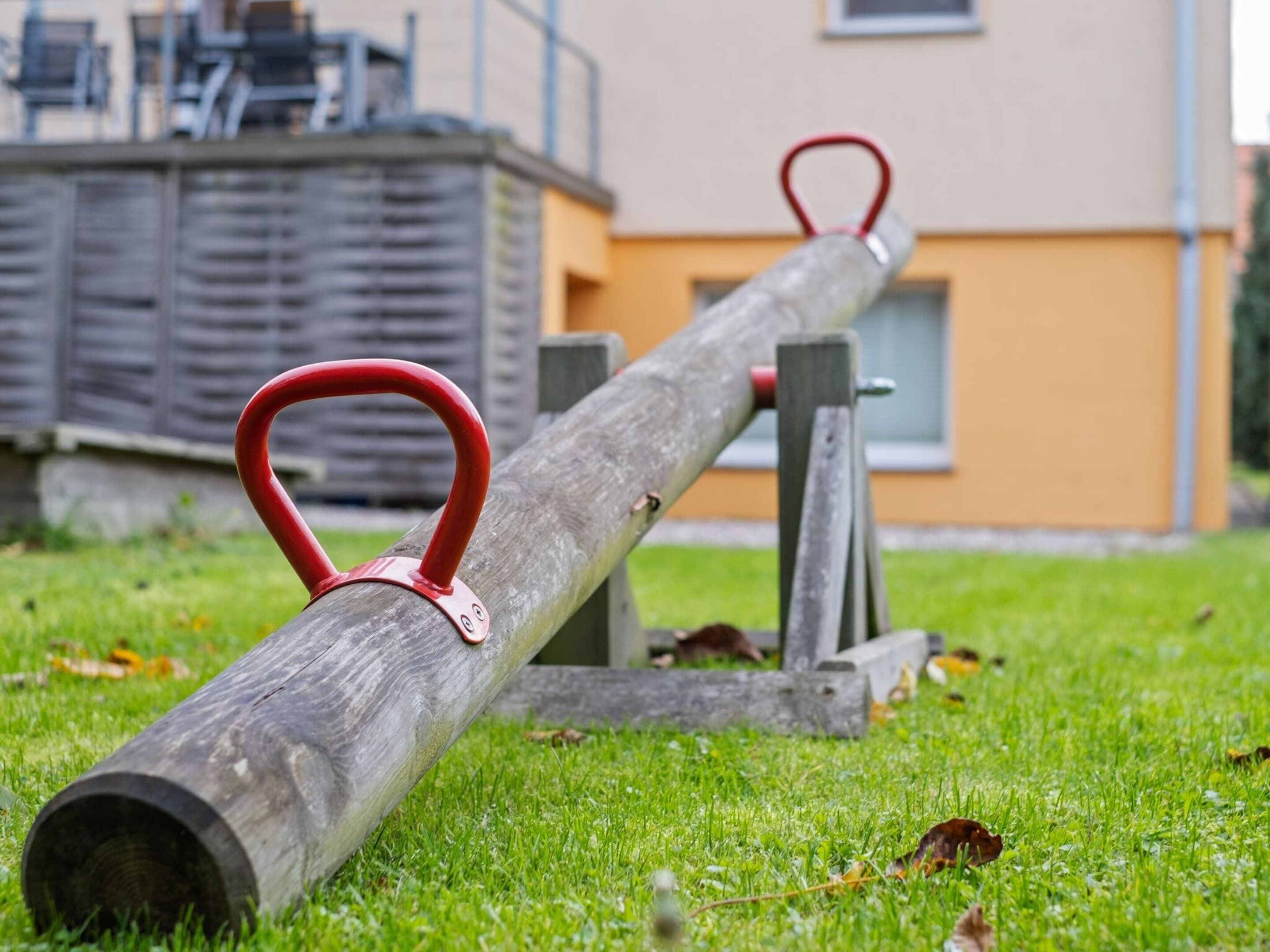 Une balançoire à bascule avec des poignées rouges, installée sur une pelouse.