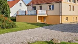 A two-story residential building with a red-tiled roof, a balcony with a white railing, and a gravel driveway. - Snug Apartment in Kalkhorst with Terrace near City Center (Kalkhorst)