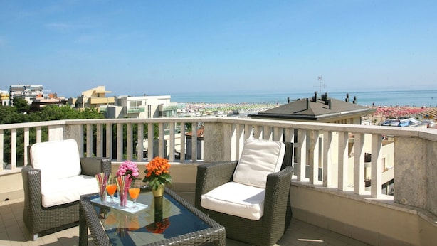 A balcony with wicker furniture, a glass table, and a view of the beach and cityscape.