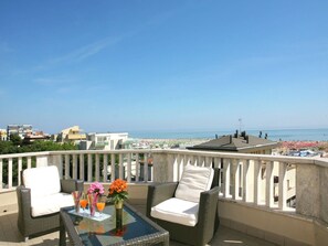 Ein Balkon mit Korbmöbeln, einem Glastisch und Blick auf Strand und Stadt.