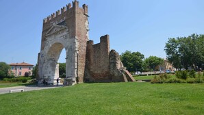 An ancient stone archway with a tower, surrounded by a grassy area and trees.
