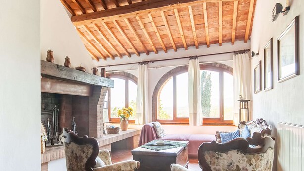 A cozy living room with a fireplace, floral armchairs, and a wooden ceiling. - Scenic Farmhouse in Peccioli with Swimming Pool near Lakes (Peccioli)