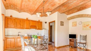 A kitchen with wooden cabinets, a dining table with chairs, a TV, and a decorative plant. - Cozy Farmhouse With Pool (Gambassi Terme)