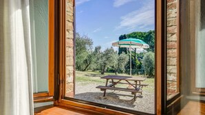 A view through a window with a wooden frame, a picnic table, and a green umbrella in an outdoor area with trees and a clear sky. - Cozy Farmhouse With Pool (Gambassi Terme)