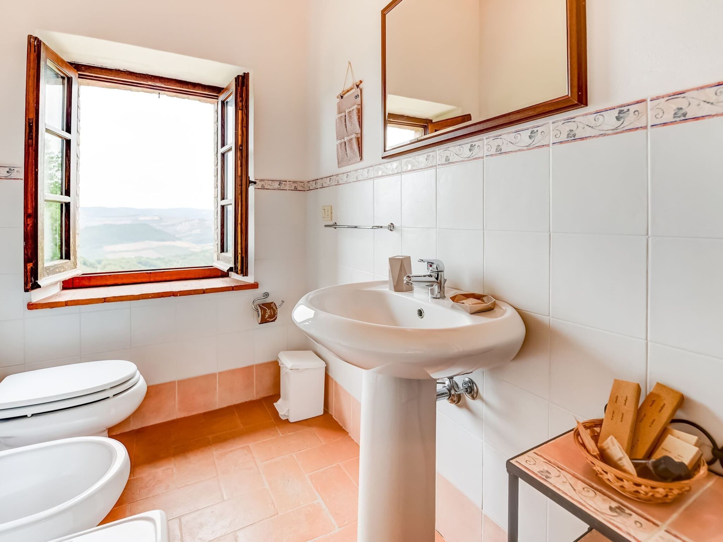 A bathroom with a toilet, sink, and window.