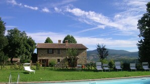 A stone building with a tiled roof, a swimming pool, and lounge chairs. - Belvilla by OYO Piandigoro - Le Querce (Radicofani)