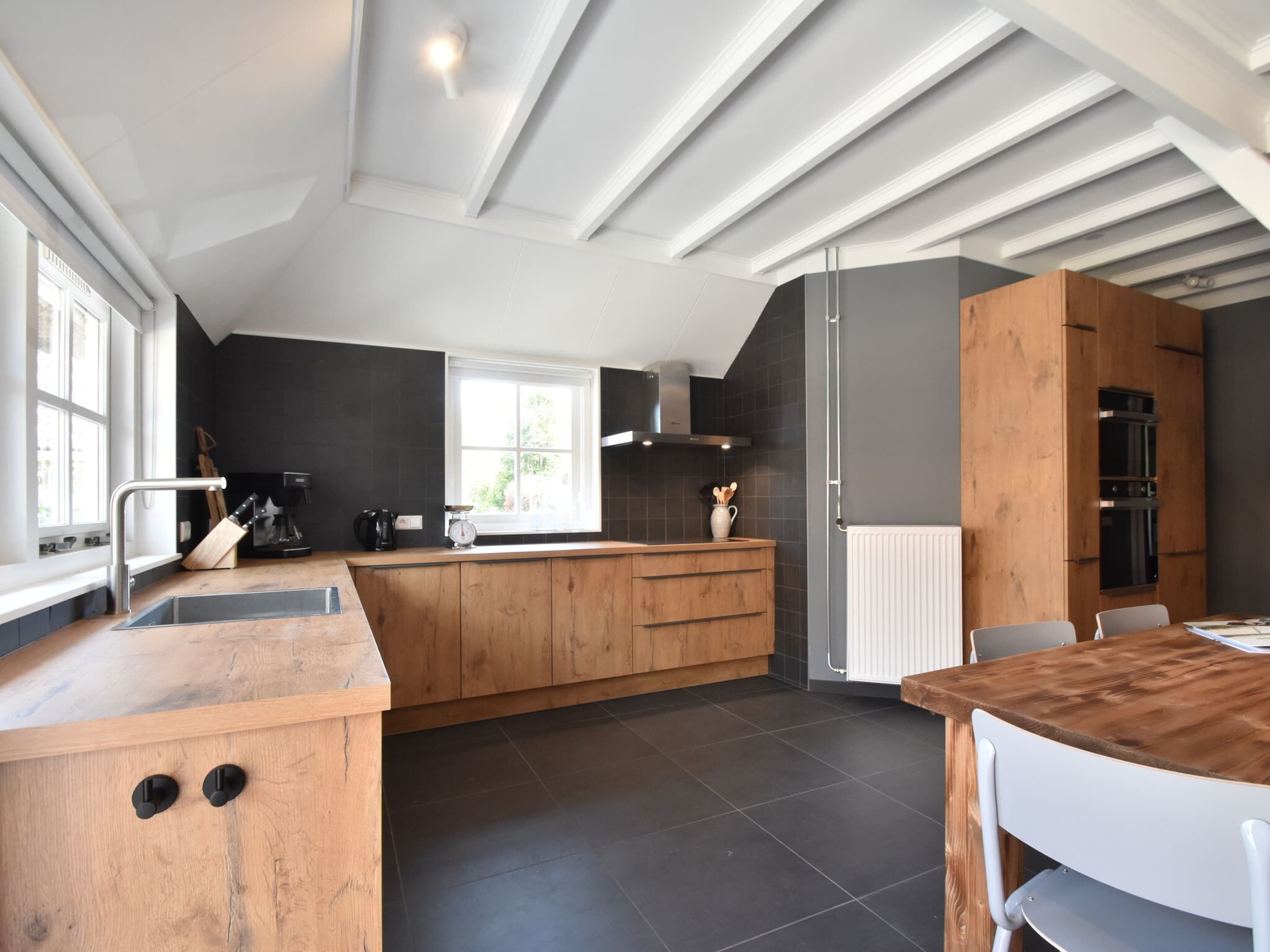Une cuisine moderne avec un îlot central en bois, un sol carrelé foncé et un coin repas comprenant une table et des chaises en bois.
