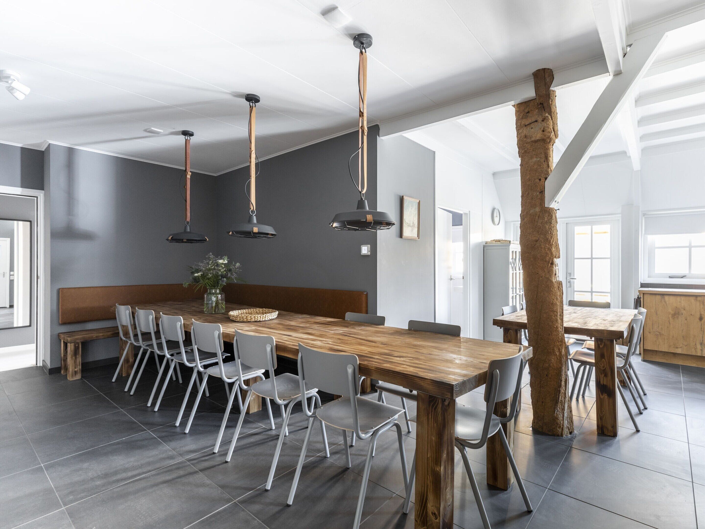 A modern dining area with a large wooden table, grey chairs, and pendant lighting.
