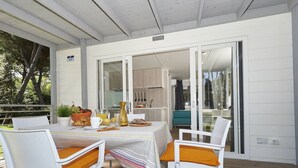 A covered outdoor dining area with a table set for two, white chairs with orange cushions, and a view into the adjacent kitchen. - Peaceful Chalet Escape (Cellole)
