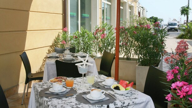 Un espace extérieur aménagé pour prendre les repas, avec des tables dressées pour le petit-déjeuner, comprenant du café, des fruits et des viennoiseries.