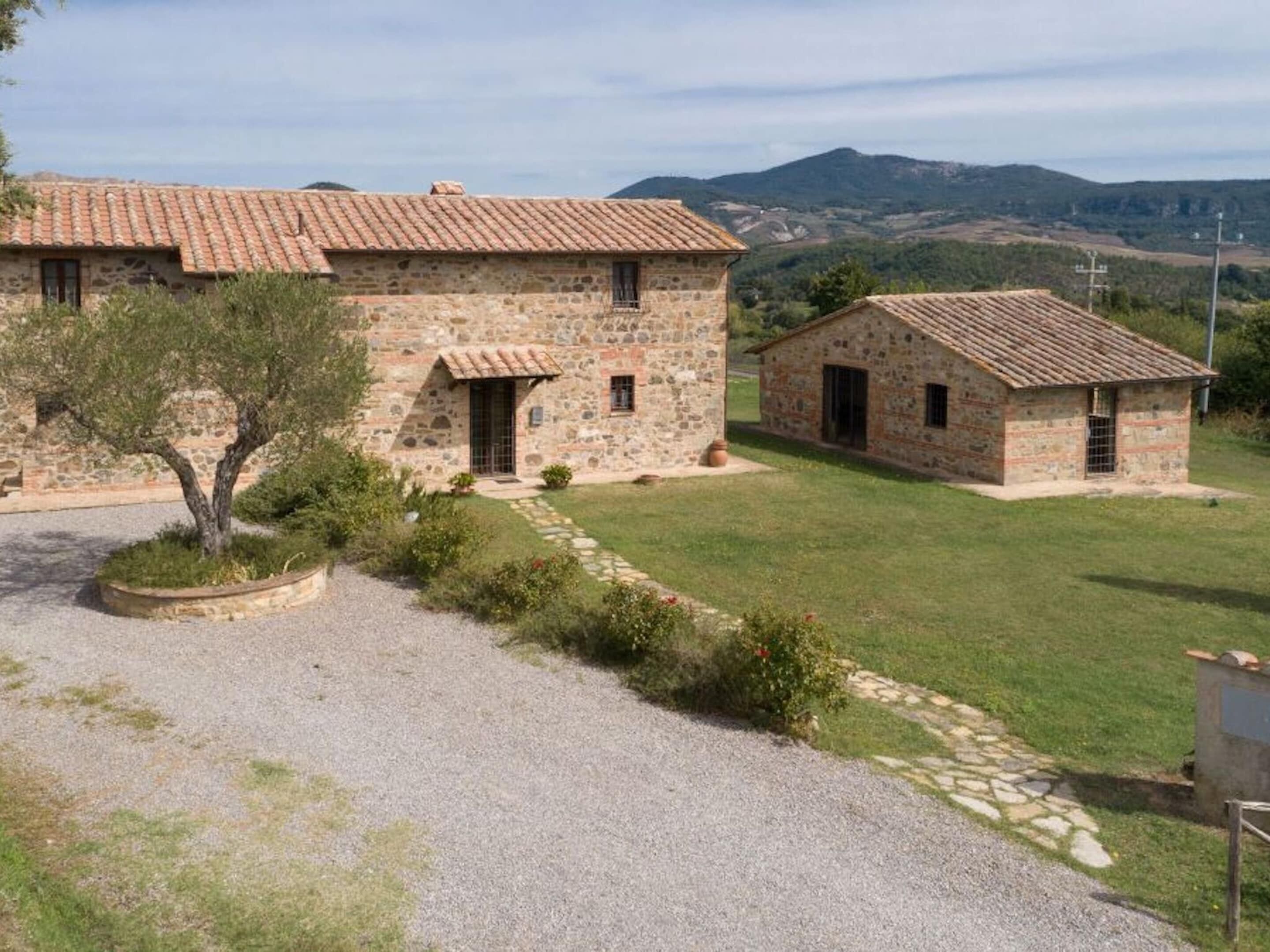 Un edificio de piedra con techo de tejas, camino de grava y césped.