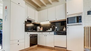 Una cocina moderna con armarios blancos, horno empotrado, microondas y cafetera.