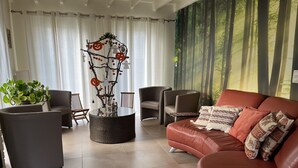Una sala de estar moderna con un sofá de cuero, dos sillones, una mesa de centro redonda y una escultura de árbol decorativa.