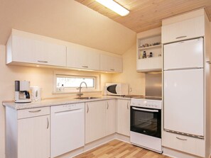 A modern kitchen with white cabinetry, a Bosch refrigerator, a Bosch oven, a Bosch coffee maker, and a window above the sink. - 6 Person Holiday Home in Humble (Sydlangeland)