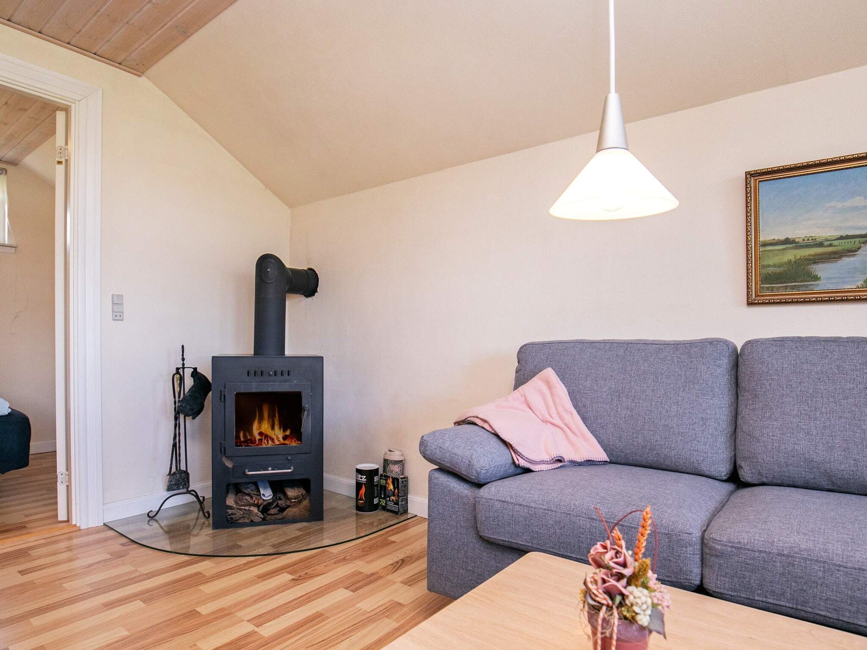 A living room with a wood-burning stove, grey sofa, wooden flooring, and a painting on the wall.