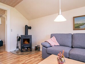 A living room with a wood-burning stove, grey sofa, wooden flooring, and a painting on the wall. - 6 Person Holiday Home in Humble (Sydlangeland)