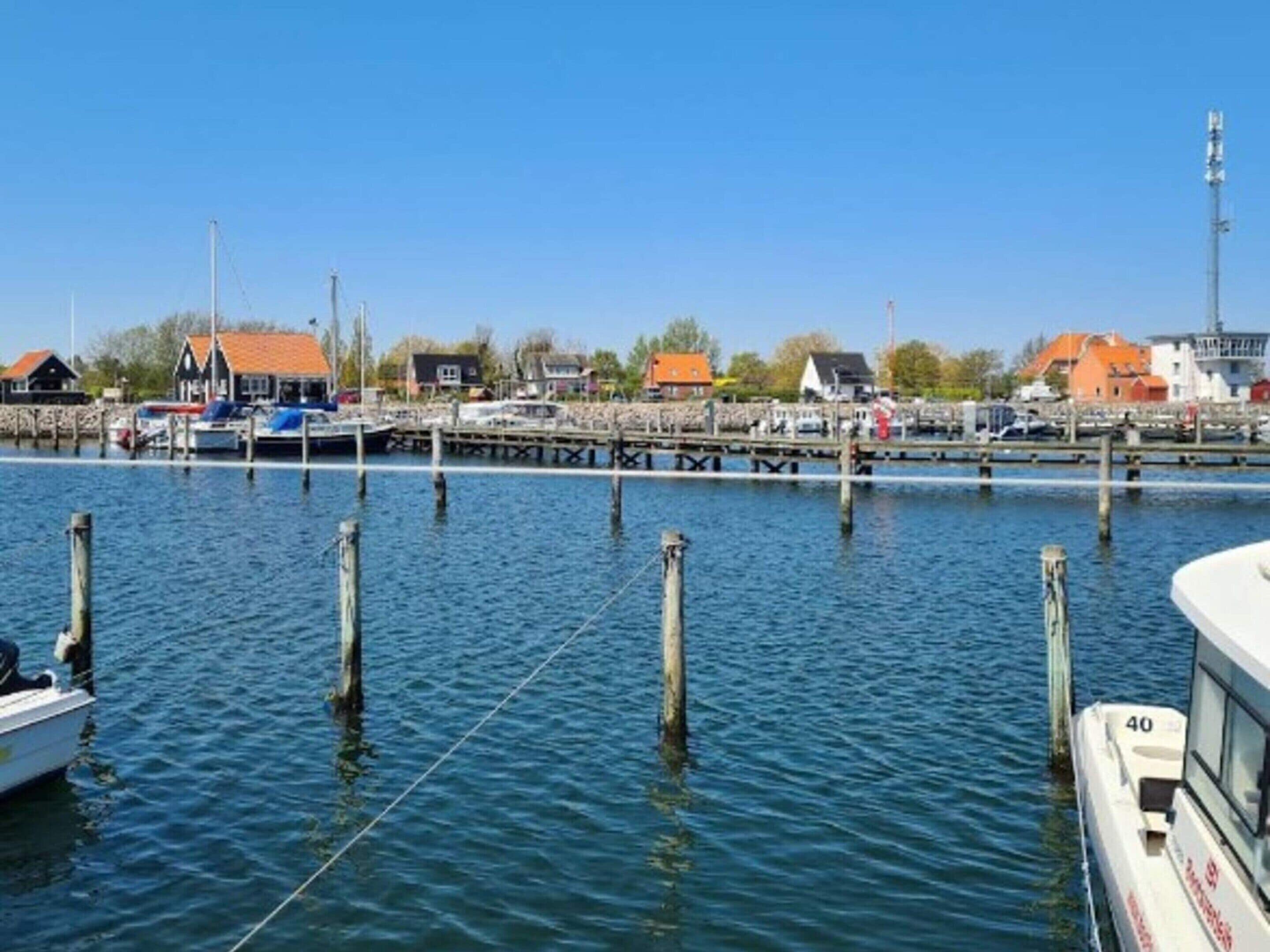 A marina with boats docked, a pier, and buildings with orange roofs in the background.