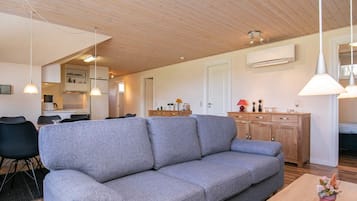 A modern living room with a grey sofa, wooden dining table, and pendant lighting.