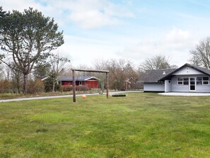 A grassy field with a swing set, a red building, and a white building with a garage. - 6 Person Holiday Home in Humble (Sydlangeland)