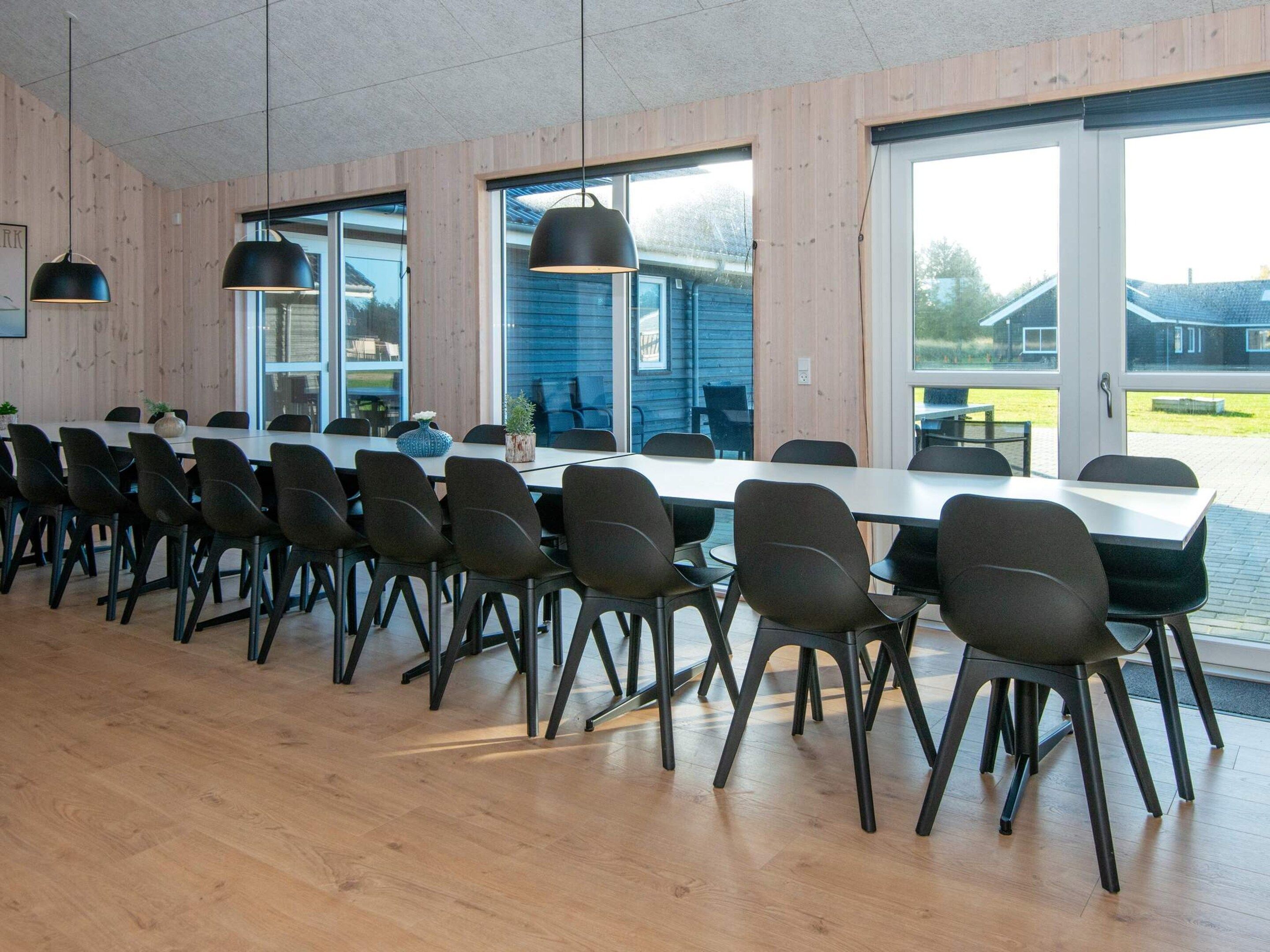 A long dining table with chairs in a room with wooden walls and large windows.