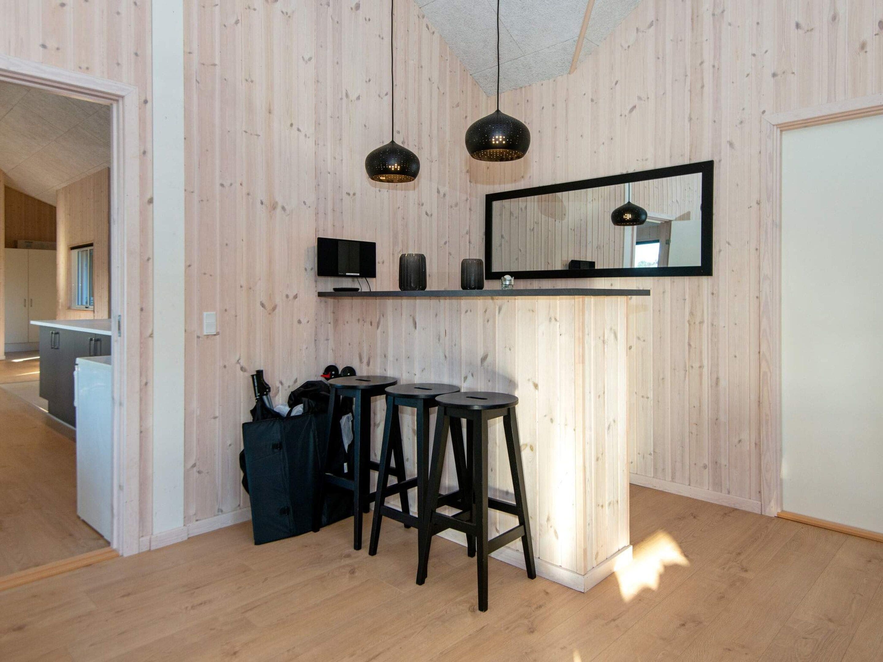 A modern kitchen with wooden panel walls, a black countertop, two bar stools, a hanging pendant light, and a mirror above the counter.