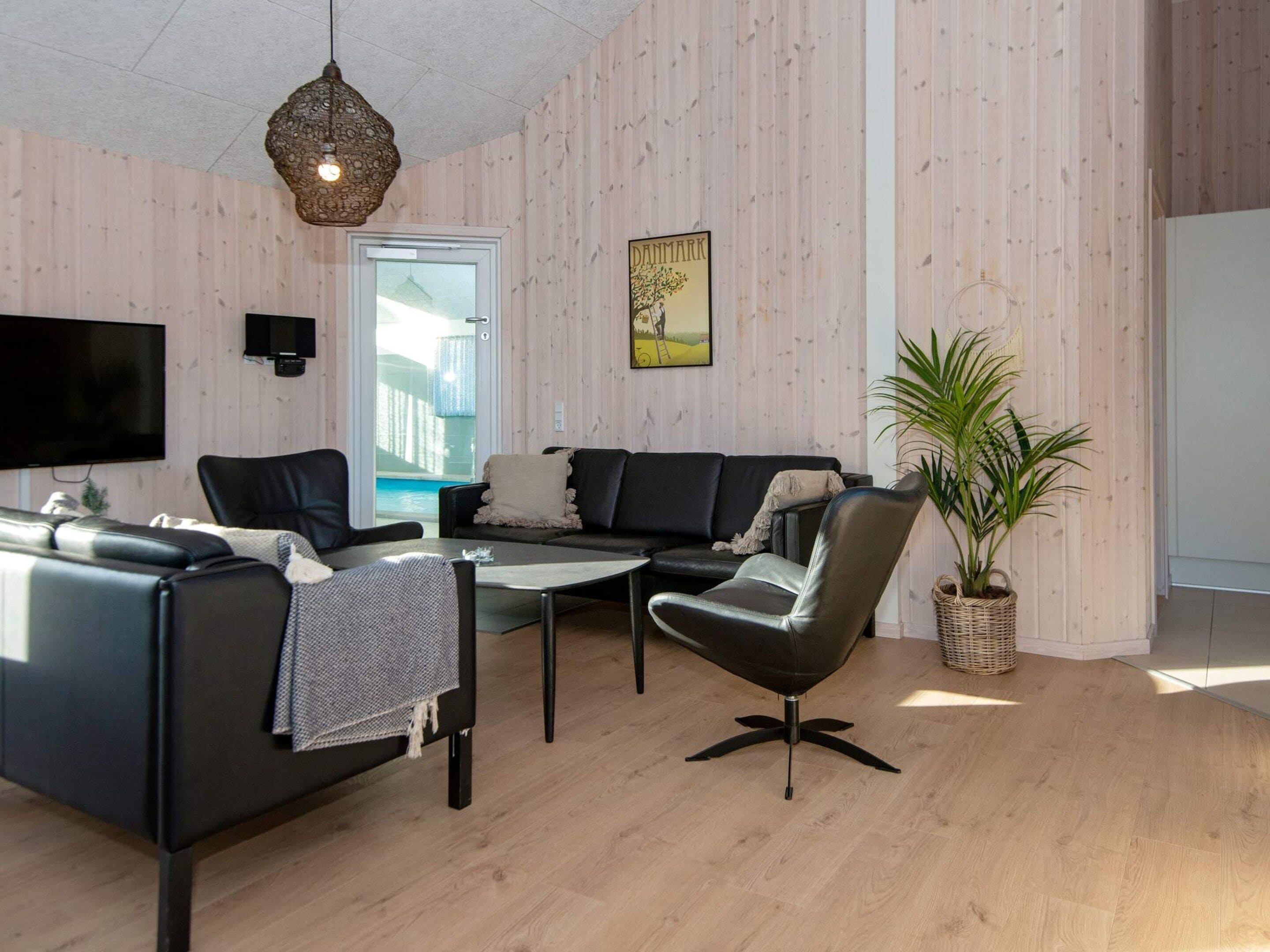 A modern living room with a flat-screen TV, leather sofas, a coffee table, and a potted plant.