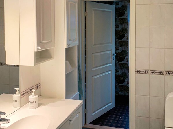 Un bagno con un lavandino bianco, due flaconi di sapone per le mani, uno specchio e una porta che dà su un ambiente piastrellato.