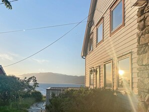 A wooden house with a stone wall, a pathway, and a view of the ocean. - 10 Person Holiday Home in Brekke (Gulen)