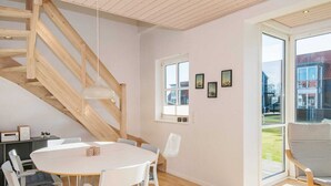 A modern interior with a wooden staircase, a round dining table with chairs, and a large window offering a view of the outside. - Holiday Home in Juelsminde (Juelsminde)