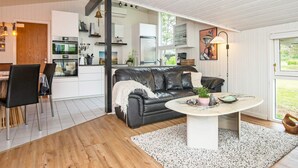 A modern living room with a black leather sofa, a round coffee table, and a dining area with a white table and chairs.