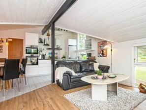 A modern living room with a black leather sofa, a round coffee table, and a dining area with a white table and chairs.