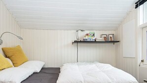 A room with two beds, a shelf with books and a lamp, and a window.