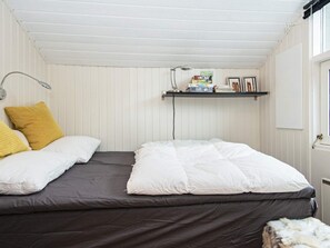 A room with two beds, a shelf with books and a lamp, and a window.